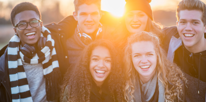 group of smiling young people at sunset
