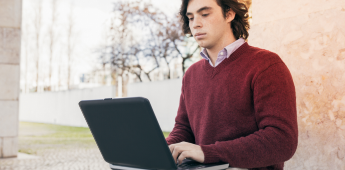young man sitting outdoors typing on a laptop